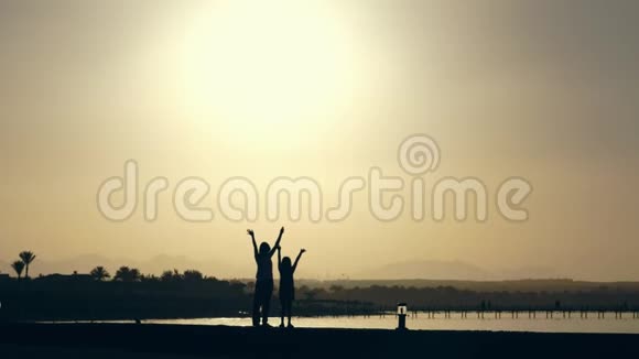 日落的夏天在海湾沿着海滩年轻的女人和十几岁的女孩正在伸手背景黑暗轮廓视频的预览图