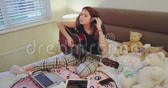 在周末女孩花时间在她的房间里弹吉他她的平板电脑和笔记本在床上视频的预览图