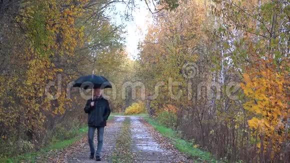 一个身材苗条的男人头发灰白戴着眼镜穿着一件黑色夹克手里拿着一把黑色雨伞走在里面视频的预览图