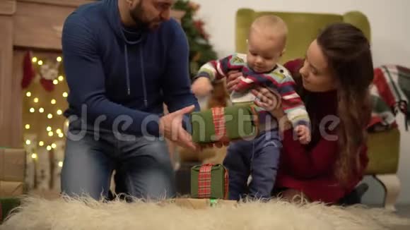 妈妈爸爸和小宝宝坐在房间的地板上装饰着圣诞节男人送小礼物视频的预览图