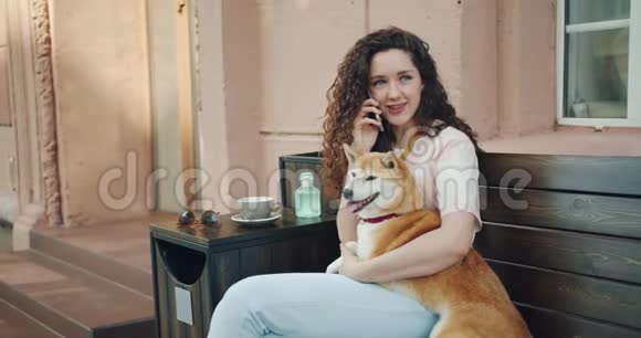 年轻的女士用手机说话在咖啡馆里抱着西巴狗视频的预览图