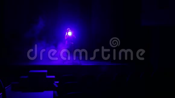 一位年轻的女照明师用烟雾引导一束从舞台的聚光灯到礼堂视频的预览图