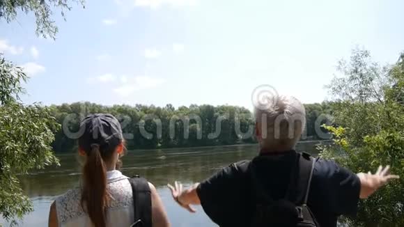 快乐旅行的概念男人和女孩一起远足带背包的徒步旅行者停在河岸上看着它他们视频的预览图
