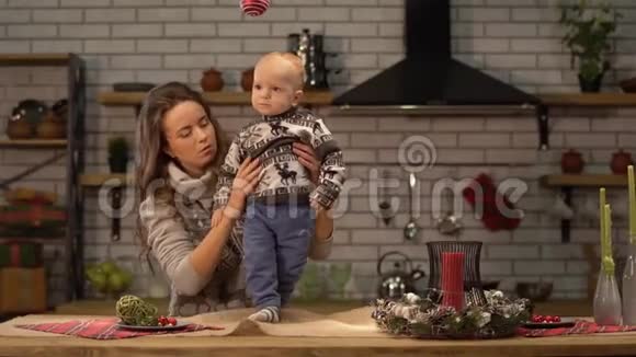 漂亮的年轻女人和可爱的婴儿在她的怀里站在现代厨房幸福的家庭观念视频的预览图