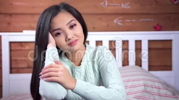 可爱温柔的年轻亚洲女孩摆姿势看着坐在卧室床上的相机视频的预览图