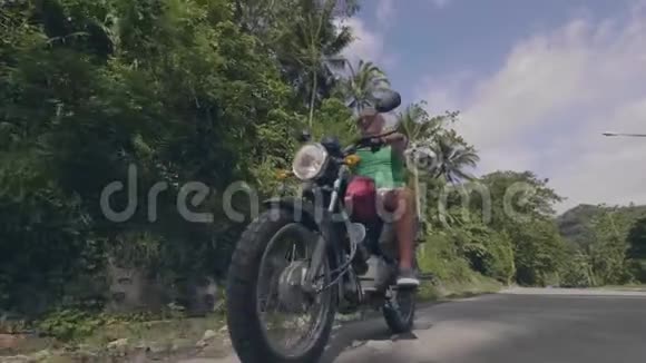 成熟的男人骑摩托车在绿色森林和蓝天背景的道路上低角度视角退休人员驾驶视频的预览图