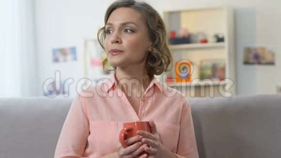 孤独悲伤的女人在沙发上喝茶思考生活困难的决定视频的预览图