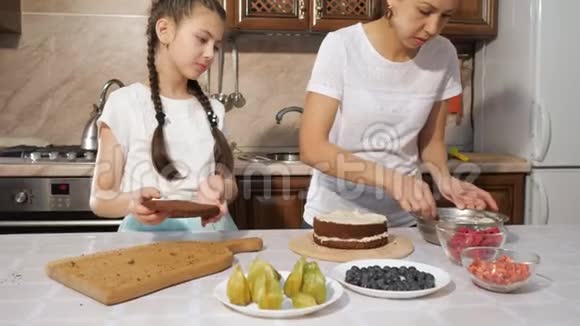 母亲和女儿用刀子在巧克力海绵蛋糕上抹上白色奶油视频的预览图