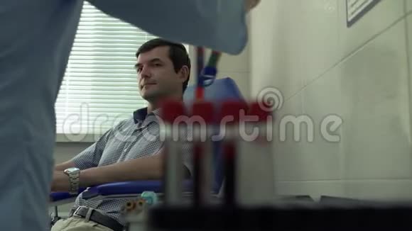 准备取背景中坐在扶手椅上的病人血液的护士的手模糊测试视频的预览图