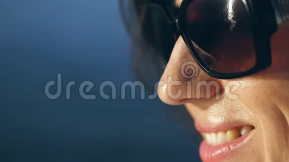 肖像一个戴太阳镜微笑的女人的轮廓阳光反射在眼镜里在蔚蓝的大海上视频的预览图