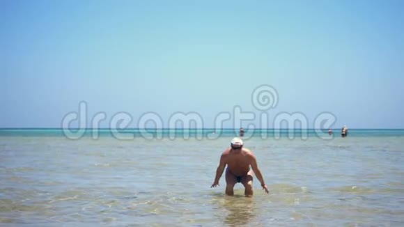 一个穿着泳裤戴着太阳镜穿着夹克的人站在浅水中在阳光下飞溅视频的预览图