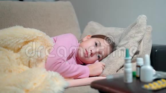 一个体温高的小女孩躺在沙发上裹着毯子卧床生病的孩子受苦的女孩视频的预览图