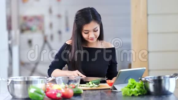 中等镜头迷人的亚洲女人在平板电脑屏幕上烹饪新鲜蔬菜沙拉视频的预览图