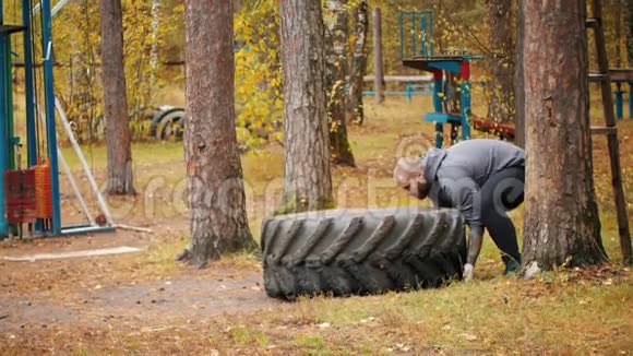一个大个子健美运动员在地板上翻轮胎并把它移到户外训练视频的预览图