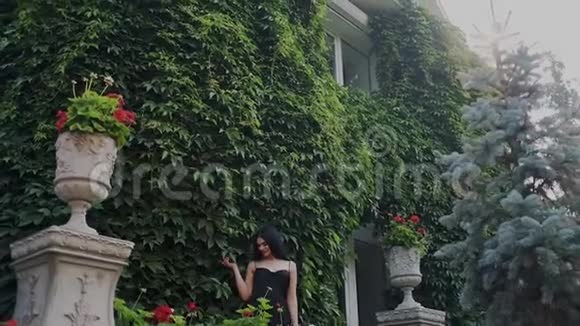 美丽的姑娘在一个豪华的大花园里赏花她靠着一堵绿色的葡萄墙吸气视频的预览图