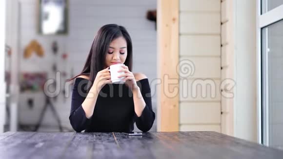 迷人的亚洲年轻女性正坐在桌子上看着窗外喝着热咖啡或茶视频的预览图