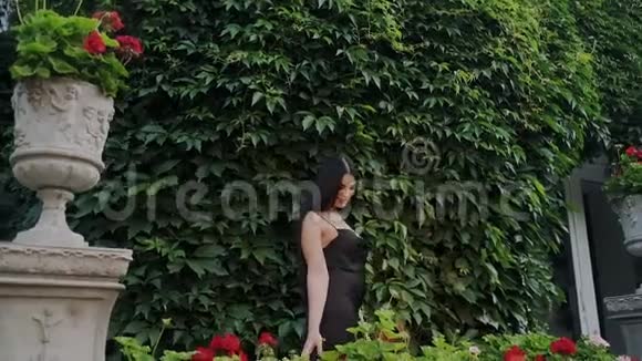 美丽的姑娘在一个豪华的大花园里赏花她靠着一堵绿色的葡萄墙吸气视频的预览图