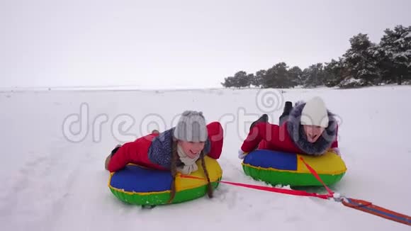 冬天穿红色夹克的孩子们骑着充气雪管和雪橇在雪中穿行运动女孩放松视频的预览图