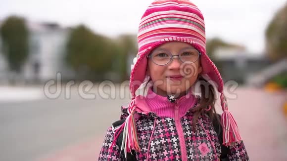 戴着眼镜和针织红帽子的微笑儿童女孩的肖像阴云密布的秋日视频的预览图