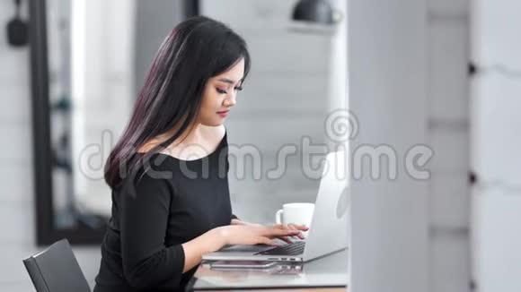 侧视可爱的年轻亚洲女性自由职业者微笑着使用笔记本电脑工作视频的预览图