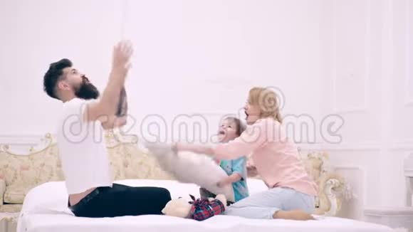 年轻的家庭在家里玩一家人在床上玩枕头大战父母花时间陪儿子视频的预览图