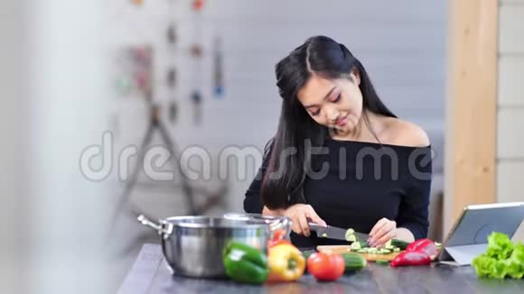 中弹漂亮的微笑年轻的亚洲女人切黄瓜坐在餐桌上厨房视频的预览图
