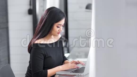 美丽的亚洲年轻女商人用笔记本电脑在办公室侧视键盘打字视频的预览图