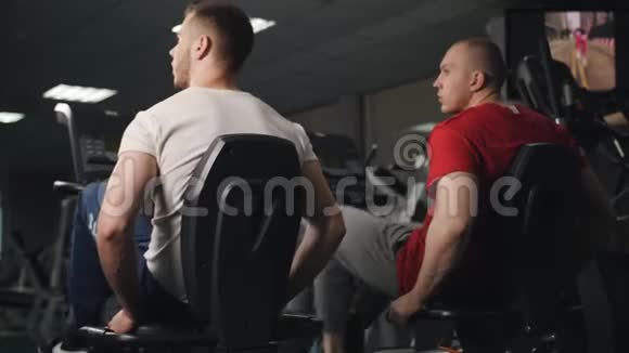 两个健身男子在健身房锻炼自行车从后面看视频的预览图