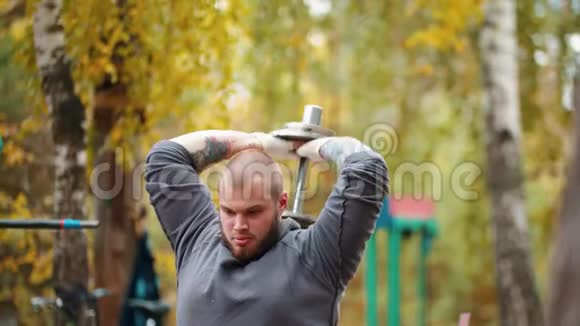 一位健美运动员用哑铃在户外运动场上背背训练双手抽插视频的预览图