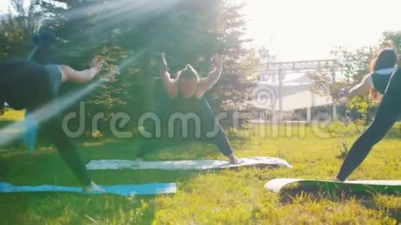 两个年轻的女人在公园里和她们的教练一起做瑜伽向前弯曲视频的预览图