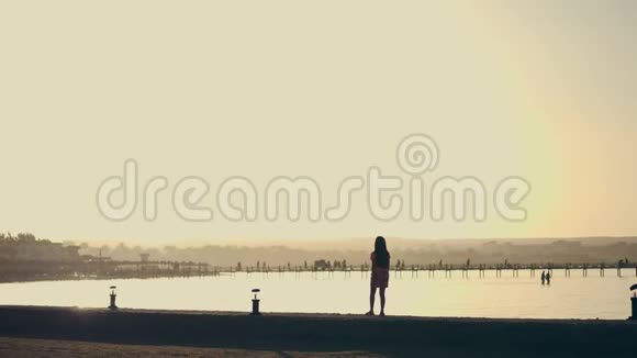 在日落的夏天在海湾里一个十几岁的女孩沿着河堤散步橙色的日落和轮廓视频的预览图