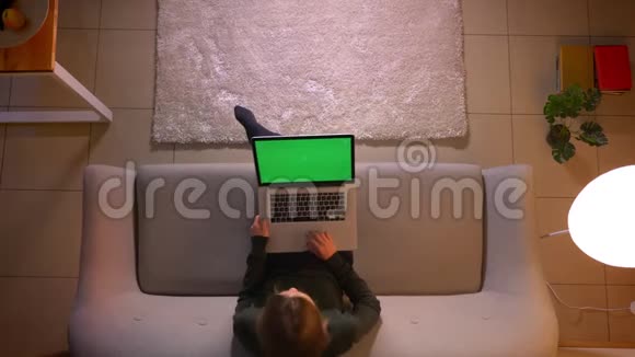 年轻漂亮的女性在笔记本电脑上用绿色屏幕浏览网页坐在室内沙发上的特写镜头视频的预览图