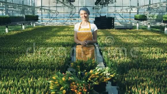 女人站在温室里戴着郁金香对着镜头微笑花生长在温室里视频的预览图
