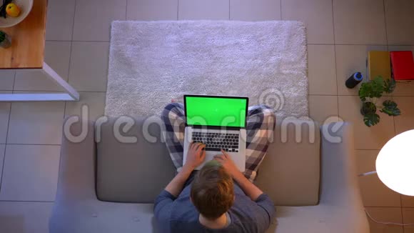 年轻男性上网学习的特写镜头在室内的沙发上坐着绿色屏幕的笔记本电脑视频的预览图