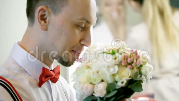 特写肖像年轻男子侧写性感打扮的新郎带着红色的蝴蝶结看着新娘他的手视频的预览图