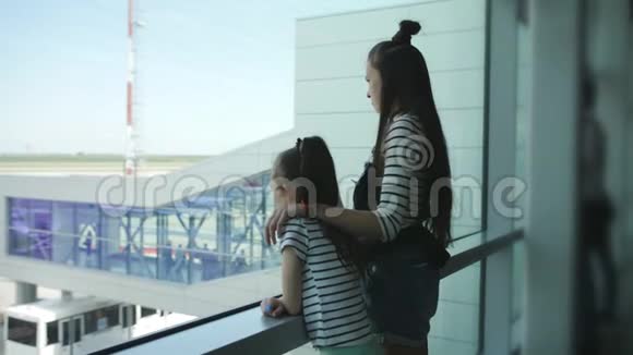 两个姐妹站在机场候机室的窗口观看飞机视频的预览图