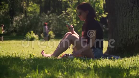 年轻女子使用智能手机在公园喝咖啡视频的预览图