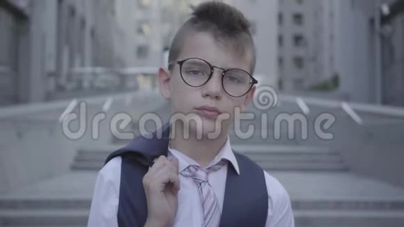 一个戴着眼镜穿得漂亮的男孩站在街上对着镜头看在美丽面前严肃的孩子视频的预览图