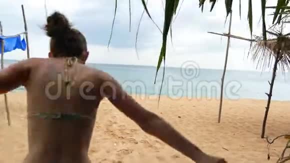 跟随年轻快乐的女人在海滩上向海洋跑去举起双手美丽的女孩在沙滩上慢跑视频的预览图