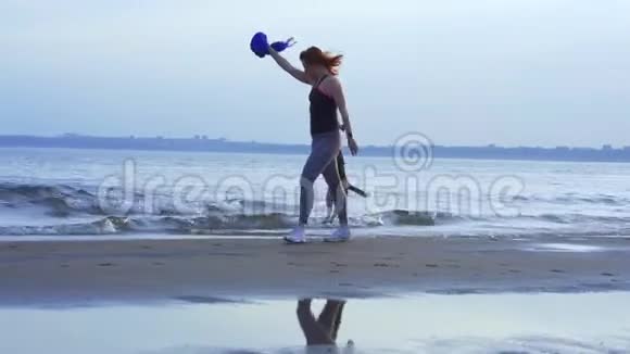 黄色动作一位中年妇女红头发穿着运动制服带着一只小狗沿着一条大河的沙岸散步视频的预览图