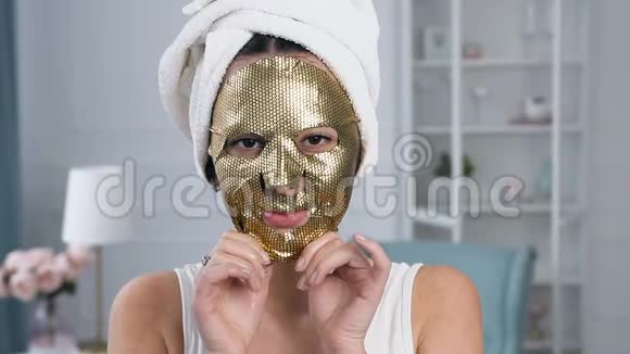年轻白种人妇女去除面部恢复活力的化妆品金色组织面具的肖像视频的预览图