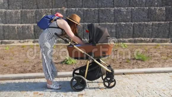 一位年轻的母亲走着试图把她的孩子从婴儿车里拿出来家庭母性和人的概念全垒打视频的预览图