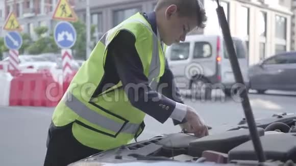 自信的小男孩穿着安全设备站在一辆破车的敞篷前修理汽车的男孩儿童视频的预览图