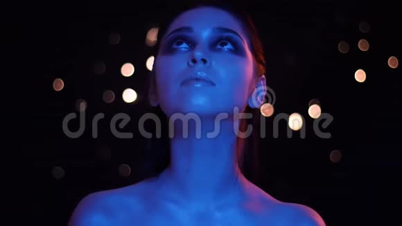 年轻漂亮的白种人女性的特写镜头裸露的肩膀上有蓝色和红色的霓虹灯和bokeh背景视频的预览图