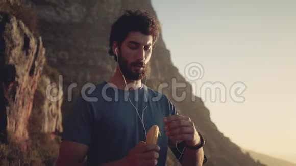 徒步旅行者吃香蕉听音乐在山上与天空对抗视频的预览图