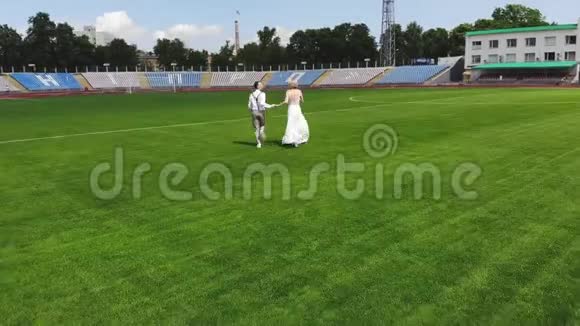 空中视频在体育场在一个绿色足球场的中心新婚快乐的新婚夫妇正在跑步视频的预览图