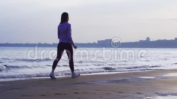 一个苗条的黑发女人沿着一条大河的沙岸散步视频的预览图