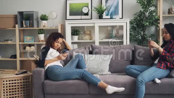 穿休闲服装的女性朋友正在公寓里使用坐在沙发上的智能手机现代技术青年视频的预览图