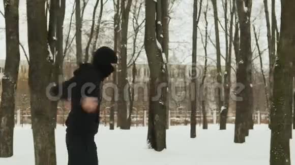 一个穿着黑色运动服和巴拉克拉瓦的年轻人在一个冰雪覆盖的城市训练前做热身运动视频的预览图