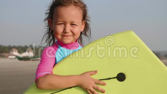 沙滩上拿着冲浪板的小女孩冲浪者的肖像视频的预览图